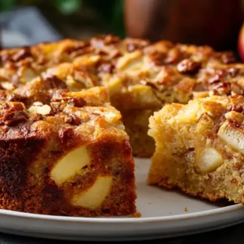 moist apple cake with large apple chunks and pecan topping on white plate