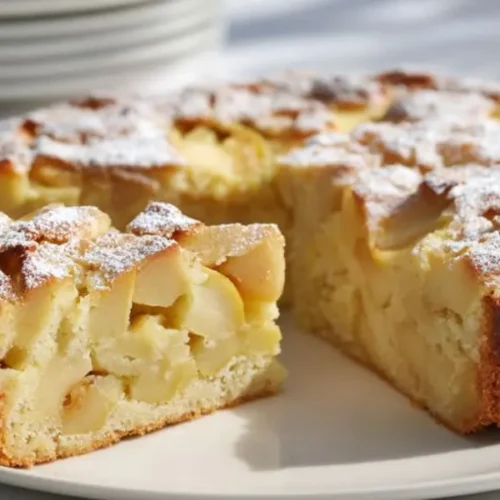 homemade apple cake with powdered sugar topping and soft apple chunks on plate