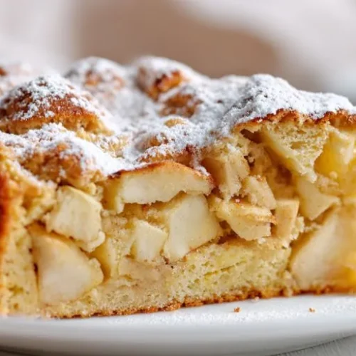 Fresh apple cake slice with powdered sugar on white plate