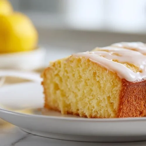moist lemon cake slice with glaze icing on top served on white plate