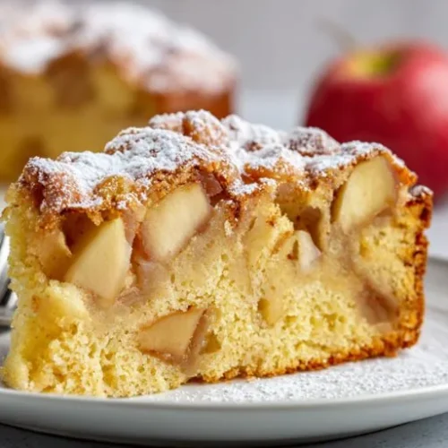 slice of vegan apple cake with fresh apple chunks and powdered sugar on a plate