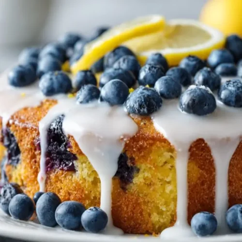 blueberry lemon cake with white glaze dripping over sides topped with fresh blueberries and lemon slices