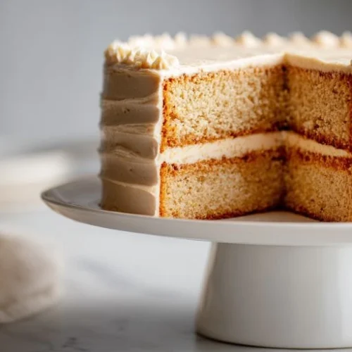 Nutty butter layer cake with creamy butter frosting and a smooth buttercream filling displayed on a white cake stand.